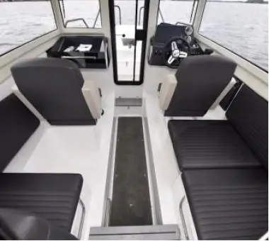 Interior of a boat featuring black seating, a central walkway, and a steering console with gauges and controls.